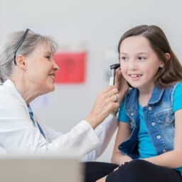 Cheerful senior pediatrician uses an otoscope to check patient's ear during medical examination.