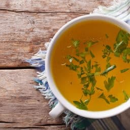 Tasty meat broth with parsley in a white bowl closeup. horizontal view from above
