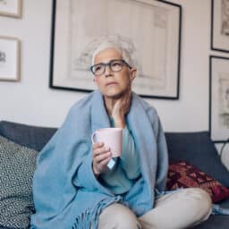 Woman with throat pain resting and drinking some tea to ease her discomfort.