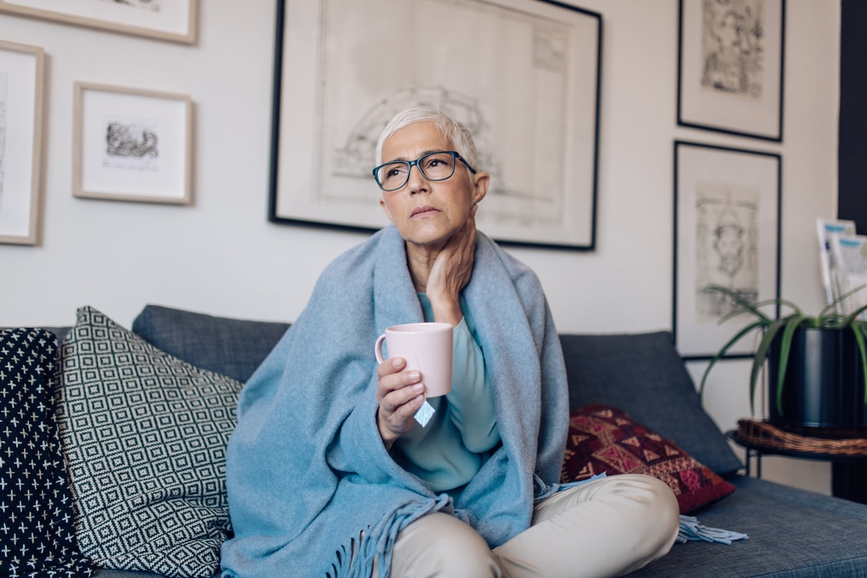 Woman with throat pain resting and drinking some tea to ease her discomfort.