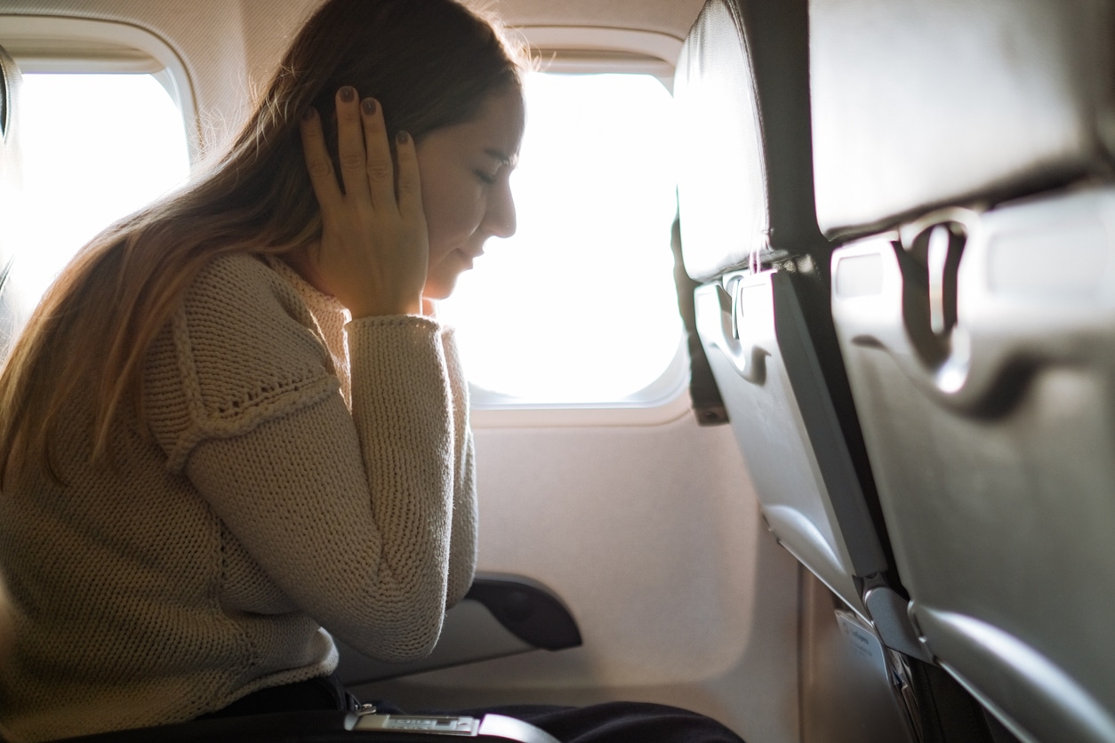 Woman covering her ears in an airplane due to ears popping.