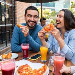 Group of happy friends eating pizza at an outdoor table