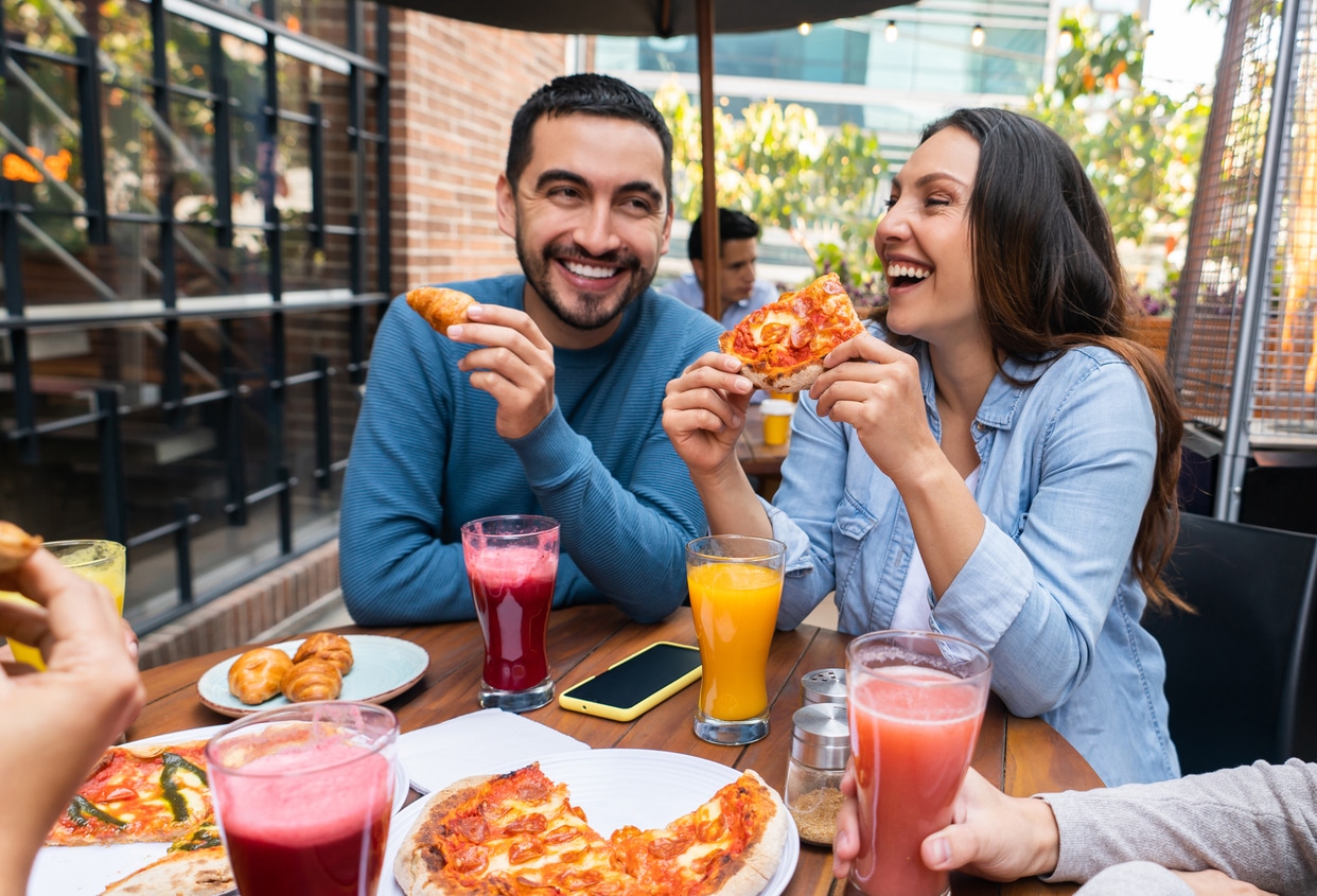 Group of happy friends eating pizza at an outdoor table