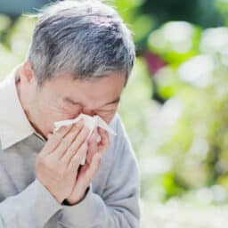 Man in a park blowing his nose with a tissue