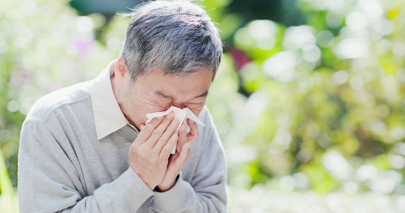 Man in a park blowing his nose with a tissue