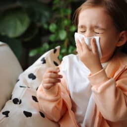 Small child with a cold or allergies blowing their nose into a tissue on a couch