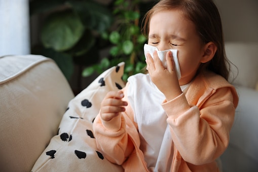 Small child with a cold or allergies blowing their nose into a tissue on a couch
