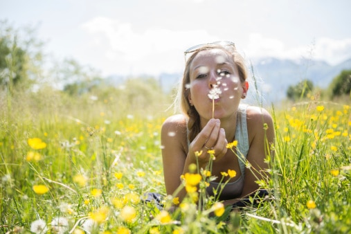 Woman in a wildflower meadow blowing dandelion seeds, unaffected by allergies thanks to immunotherapy