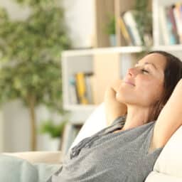 Woman relaxing at home, arms behind her head, breathing in