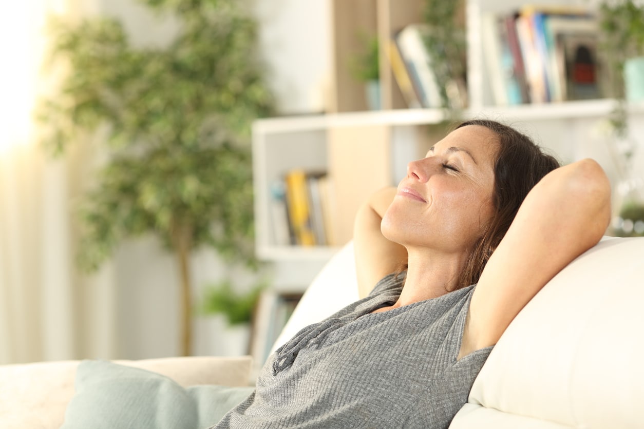 Woman relaxing at home, arms behind her head, breathing in